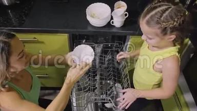 妈妈教女儿聪明的女孩学习使用洗碗机。 年轻的女主人孩子们在装脏盘子